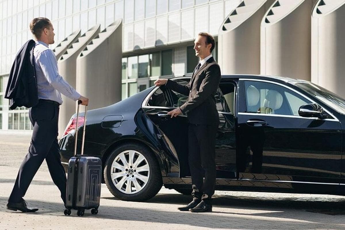 Professional chauffeur in suit standing by luxury sedan