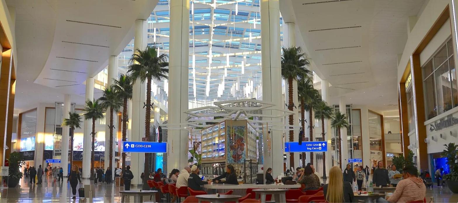 Palm-lined Terminal C atrium at Orlando International Airport (MCO), with travelers, seating and signs pointing to gates and baggage claim.
